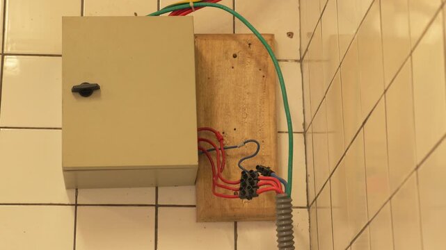 Electrical junction box mounted on a light brown tiled wall with exposed red and green wires in Yaound&eacute;, Cameroon. Static close-up shot.
