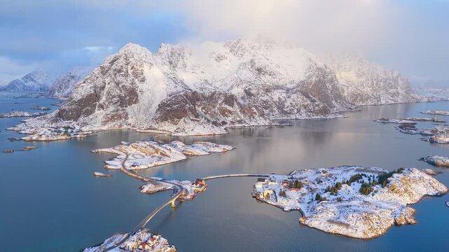 Breathtaking cinematic aerial drone shot of snowy Norwegian peaks and coastal bridges in Lofoten during winter golden hour. Great for travel and nature documentaries.