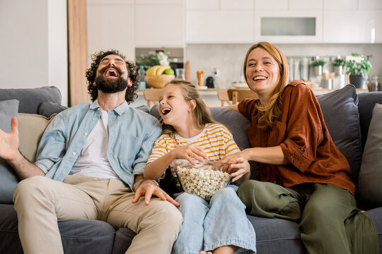 Family laughing together watching movie at home on sofa