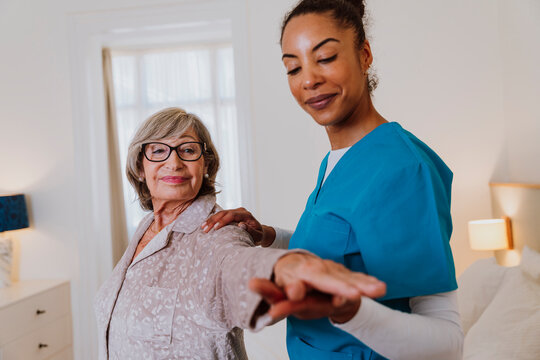 Nurse assisting woman with arm movements for rehabilitation at home