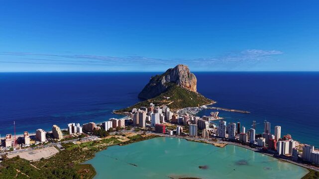 Panoramic view of Calpe, Spain featuring the iconic Penon de Ifach rock formation rising from the Mediterranean Sea, with the coastal city, lagoon and marina visible below