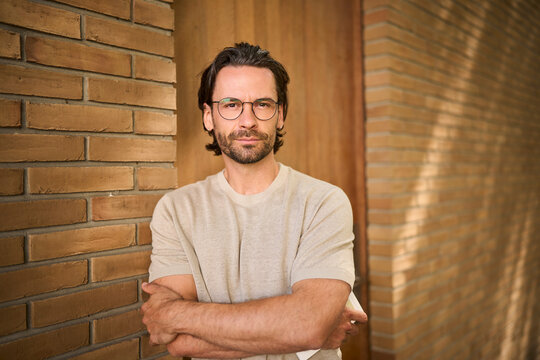 Confident man with glasses standing in front of brick wall indoors