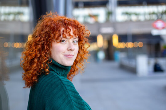 Smiling portrait of a a woman with curly red hair in green sweater outdoors