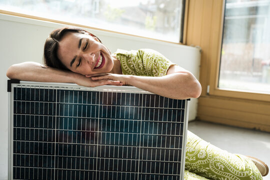 Smiling mature businesswoman with eyes closed leaning on solar panel at office