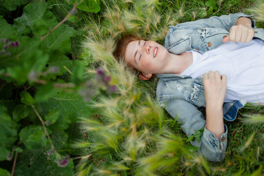 Teenage girl with red hair relaxing in summer meadow