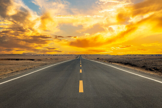 Straight asphalt highway through desert landscape under dramatic golden sunset sky, Xinjiang, China