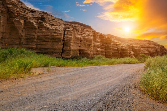 Sandy road through yardang landform with green grass under sunset sky in Xinjiang, China