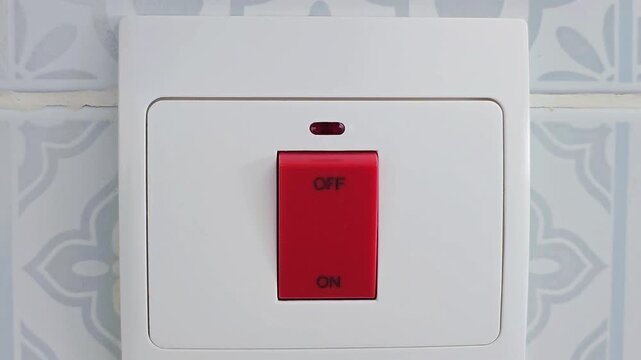 Close up of human finger pressing red electric light switch turning on power on white wall background, household electricity control, safety and energy concept