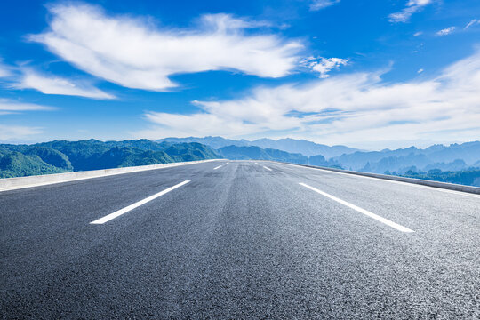 Empty straight asphalt highway leading to a distant mountain range under a blue sky