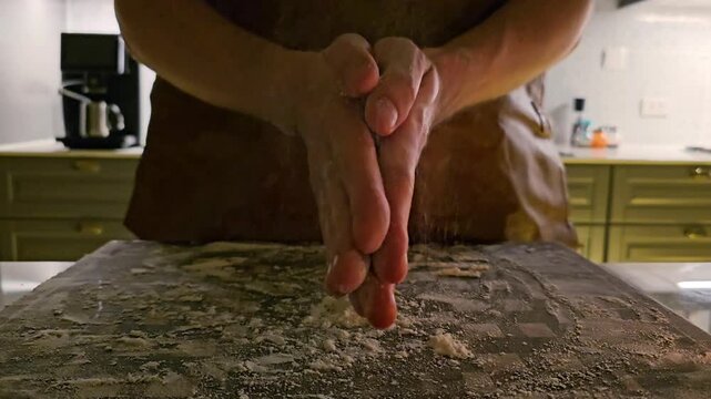 Close up of hands clapping flour over kitchen table, dough preparation process with flying flour particles, home cooking and baking activity in domestic kitchen interior