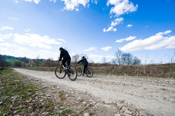 Fototapeta premium Two cyclists enjoying a sunny day on a gravel road, surrounded by nature. A perfect outdoor adventure.