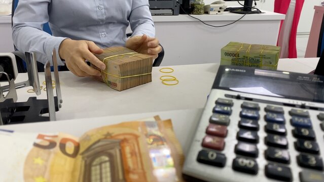 Financial professional bundling thick stacks of vietnamese dong with yellow rubber bands on a white counter, calculator and blurred euro notes hinting at currency exchange and accounting