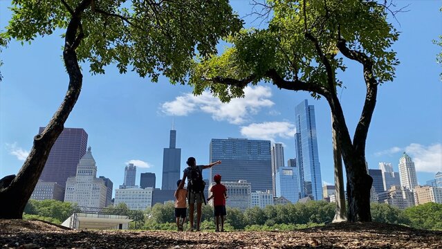 Family group standing with parent pointing toward the chicago downtown urban skyline, appreciating the cityscape view from millennium park on a clear sunny day