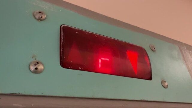 Red led floor display cycling numbers on turquoise metal panel closeup shows worn screws and illuminated arrows as maintenance