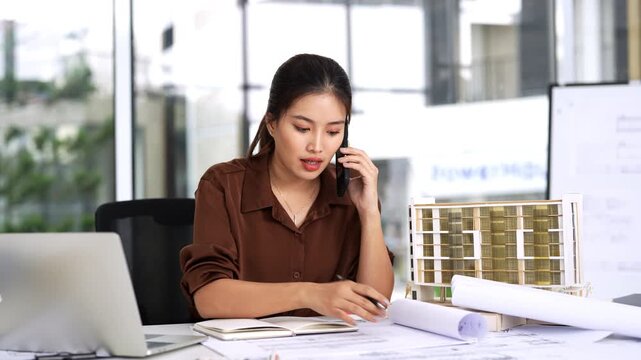 Female Civil Engineer Construction professional reviewing shop drawing of structural floor plan  and communicates on smartphone in an office.