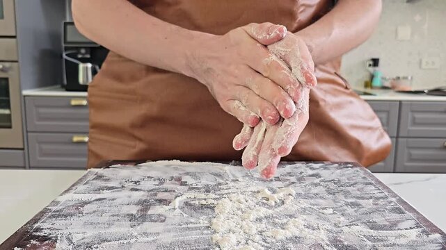 Close up of baker hands clapping flour over kitchen table creating flour dust cloud, slow motion baking process with dough preparation in home kitchen, food cooking and pastry making concept