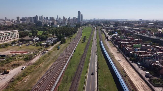 Drone tracks right as a commuter train moves forward through Recoleta, revealing the Law Faculty building and the modern Buenos Aires city skyline