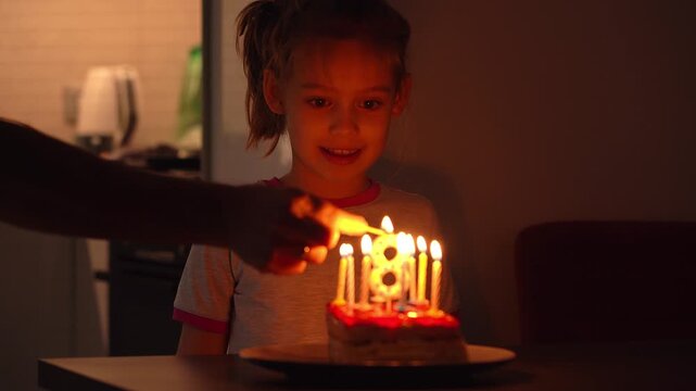 Happy girl blows out burning candles on cake on birthday and laughs. Childs Birthday celebration. Close up