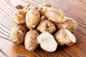 Fototapeta premium Freshly harvested Jerusalem artichoke (sunchoke) tubers with a yellow flower and green leaves, arranged on a rustic wooden table.