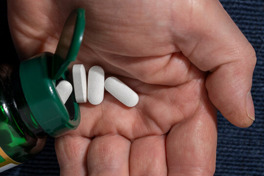 Pouring pills from a bottle into a hand. Closeup of white caplets being poured from green plastic bottle into human palm. Concept of healthcare medication intake supplements or daily vitamin routine