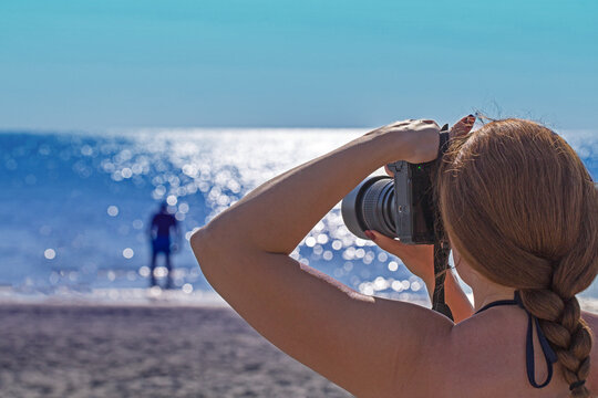 Woman takes picture of man on beach during sunny day by ocean