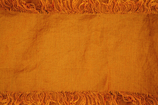 Warm orange fabric with textured pattern and frayed edges laid out on flat surface for textile display