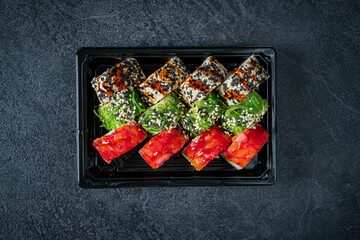 Colorful sushi rolls arranged artfully on a black plate with a textured background
