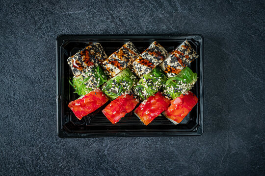 Colorful sushi rolls arranged artfully on a black plate with a textured background