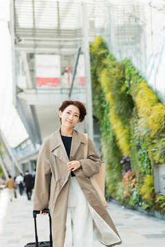 トレンチコートを着てキャリーバッグを引く30代ビジネス女性