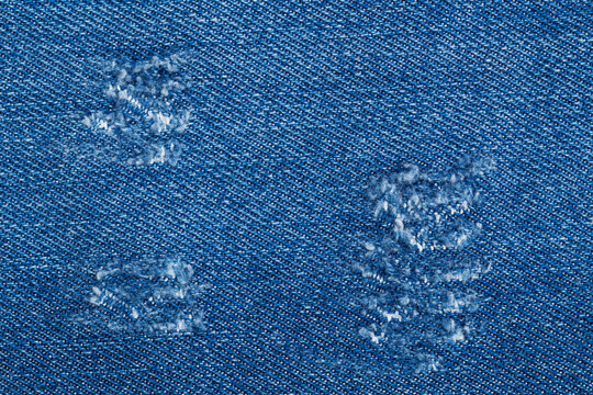 Details of worn denim fabric with frayed patches showing wear and tear in casual style