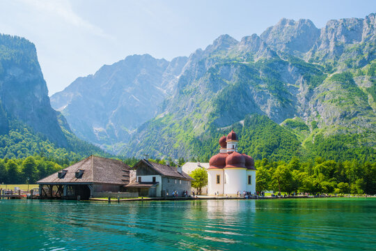 The historic St. Bartholoma pilgrimage church with its red onion domes stands on the shore of Konigsee lake against the backdrop of the Bavarian Alps in Berchtesgaden National Park, Germany.