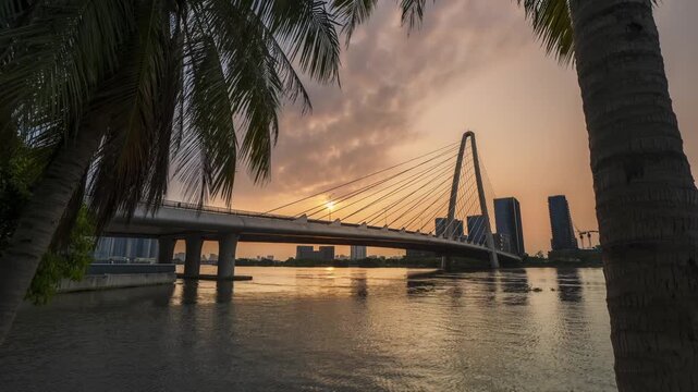Beautiful sunset timelapse of Thu Thiem 2 cable-stayed bridge in Ho Chi Minh City, featuring palm trees and reflections.
