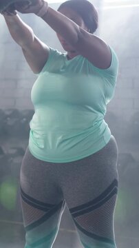 Vertical video: Gripping kettlebell, woman in mint top doing kettlebell swings in gym for fitness