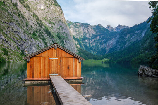 Iconic wooden boathouse on the shore of Obersee lake with a stunning backdrop of the high Alps in Bavaria, Germany near Konigssee.
