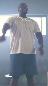 Vertical video: Starting warmup man wearing tee, watch in gym doing side-bend and crossarm stretch