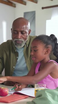 Vertical video: Pointing girl in pink tank writing in notebook at kitchen grandpa guiding homework