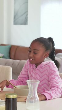 Vertical video: Responding kid in pink hoodie reaching jar near bowl in kitchen to offscreen voice