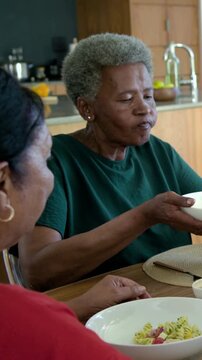 Vertical video: Holding senior lady in green tilting white bowl to mouth in kitchen serving pasta