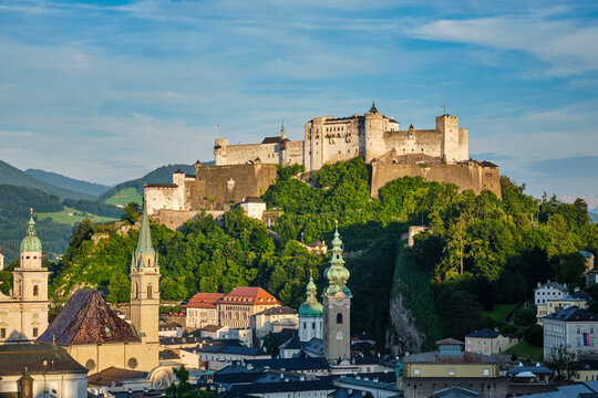 A high-angle daytime view of the medieval Hohensalzburg Fortress and the baroque church domes of the historic old town in Salzburg, Austria.
