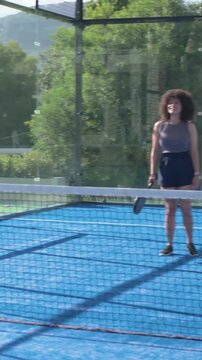 Woman stepping after incoming ball, hitting shots with paddle near net on padel court training