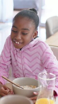 Vertical video: Hearing offframe voice, girl in pink hoodie holding bowl at dining table glancing
