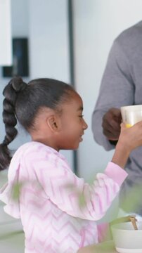 Daughter reaching for orange juice at counter for health, father placing mug, she covering ear