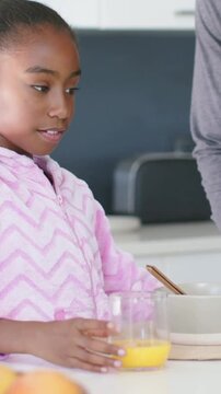 Adult bringing bowl serving breakfast prompts child reaching for glass OJ as camera panning counter