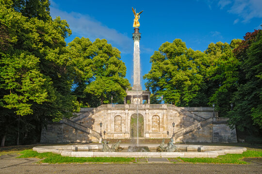 Wide angle view of the Friedensengel monument with a golden angel statue and rising fountain water in Munich, Bavaria, Germany at dusk.