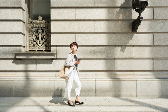 石造りの建物の前を歩く30代ビジネス女性