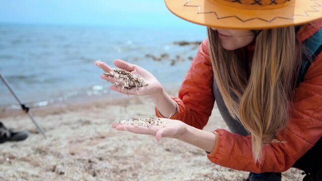 close-up of woman examining shell sand texture in hands on lake shore, detailed natural pattern of crushed shells, outdoor exploration, travel lifestyle, tactile experience and nature study concept
