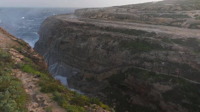 Powerful Waves Crashing Through Narrow Rocky Inlet Of Wied il-Mielaħ Window On Gozo Island, Malta. drone shot