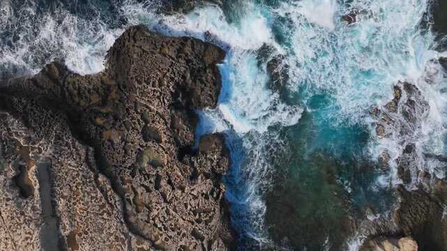 Cinematic aerial top down shot of powerful turquoise ocean waves hitting a rugged rocky coastline. Perfect for travel and nature documentaries. Sea level rise and climate change concept