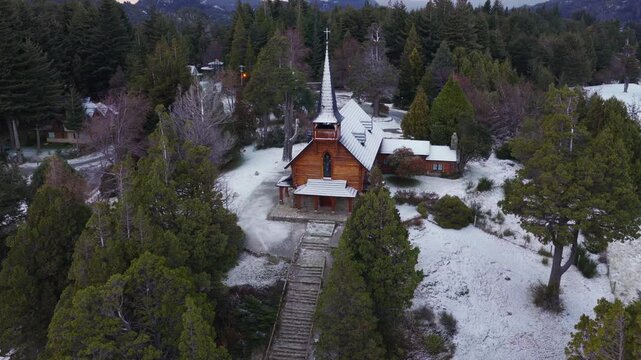 Aerial view of San Eduardo Chapel in snowy Bariloche surrounded by forest and mountains in winter Argentina.
