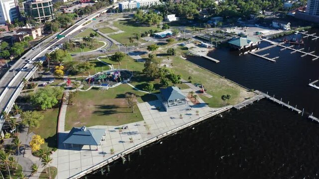A park with a playground and pavilion near a waterfront. Traffic flows on the nearby elevated road. Suitable for urban planning and recreational content.